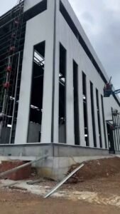 Elevador aéreo asistiendo en la colocación de paneles de pared para naves industriales de gran altura