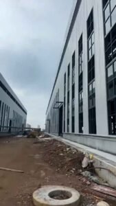 Vista del pasillo entre dos naves industriales de acero con múltiples ventanas verticales