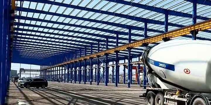 Amplia bodega industrial de acero con camión hormigonero en el interior, destacando las vigas carrileras amarillas preparadas para puente grúa.