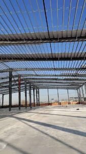 Wide clear span metal building warehouse interior showing rigid steel columns and roof purlins.