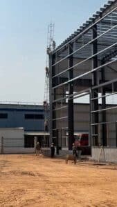 Operarios especializados trabajando en altura sobre andamios durante la construcción de la fachada de una nave industrial prefabricada.