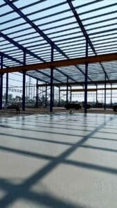 Detalle contrapicado de las correas de techo y vigas azules soportando la cubierta en bodegas logísticas.