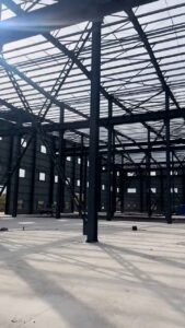 Solid steel columns forming the rigid corner of an earthquake-resistant custom warehouse storage facility, with grid shadows on the floor.
