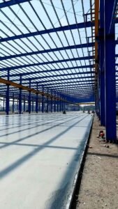 Estructura metálica principal azul para bodegas industriales con piso de concreto recién fundido