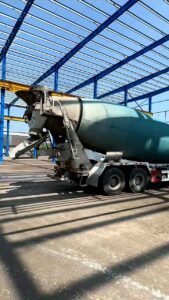 Camión mezclador de concreto ingresando marcha atrás bajo la robusta estructura azul de mega bodegas.
