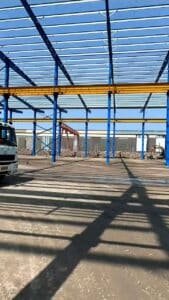 Vista lateral de un camión vertiendo concreto dentro del inmenso marco de acero de bodegas comerciales.