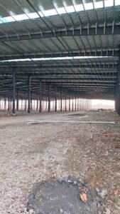 Vista exterior de proyecto casi finalizado de galpones prefabricados chinos con atractivos remates azules y muros blancos.