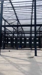 Expert worker safely securing bolted connections on the roof ridge beam of a high clearance warehouse.