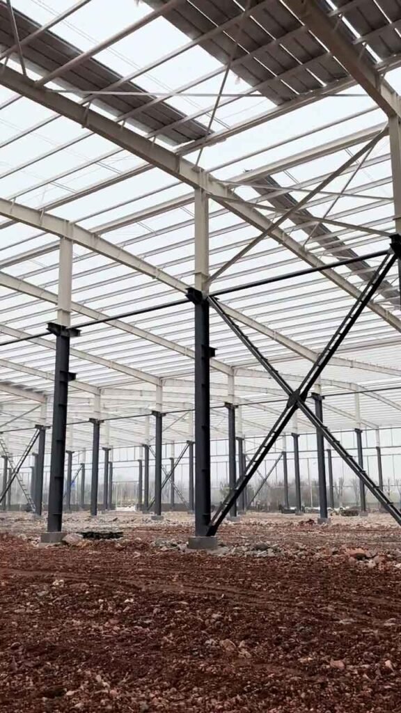Trabajadores instalando paneles metálicos rojos en la fachada exterior de bodegas de acero industriales.