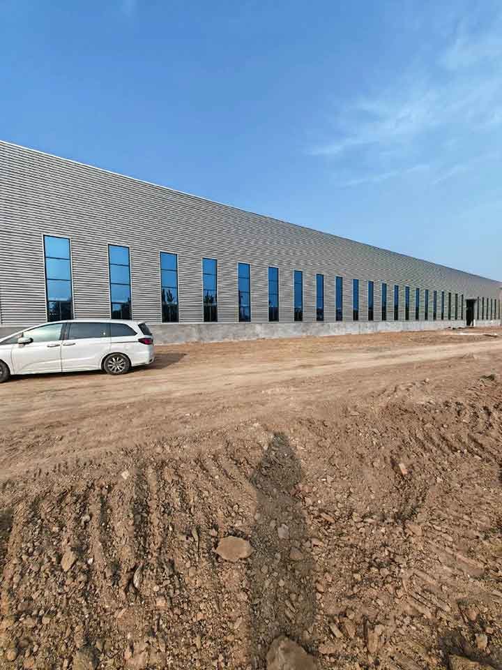 A massive prefabricated metal building warehouse with a white car parked in front for scale.