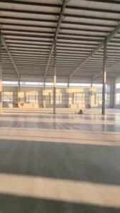 Grúa elevando vigas de techo prefabricadas durante el montaje seguro y eficiente de una bodega industrial metálica.