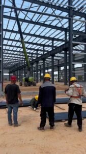 Equipo de contratistas coordinando la preparación de perfiles metálicos para el ensamblaje de una nave industrial prefabricada.