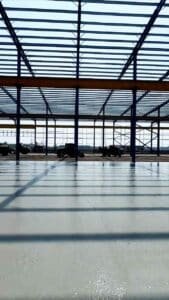 Vehículos de construcción operando cómodamente dentro de la amplia nave de bodegas metálicas en fase de obra.