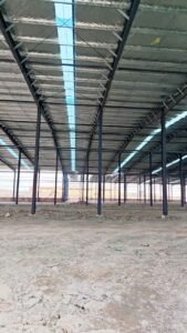 Operarios colocando las láminas de revestimiento exterior blanco en la fachada de galpones prefabricados chinos.