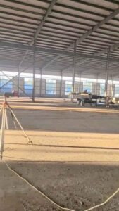 Trabajadores instalando paneles metálicos de aislamiento en la fachada exterior de una bodega industrial moderna.