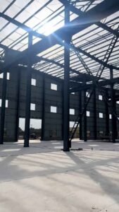 Yellow mobile crane precisely lifting a steel roof purlin during steel warehouse construction.