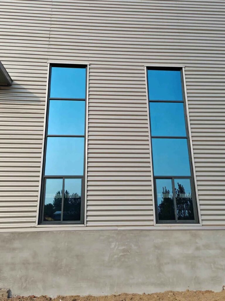 Close-up of reinforced aluminum and blue glass windows integrated into a metal building wall.