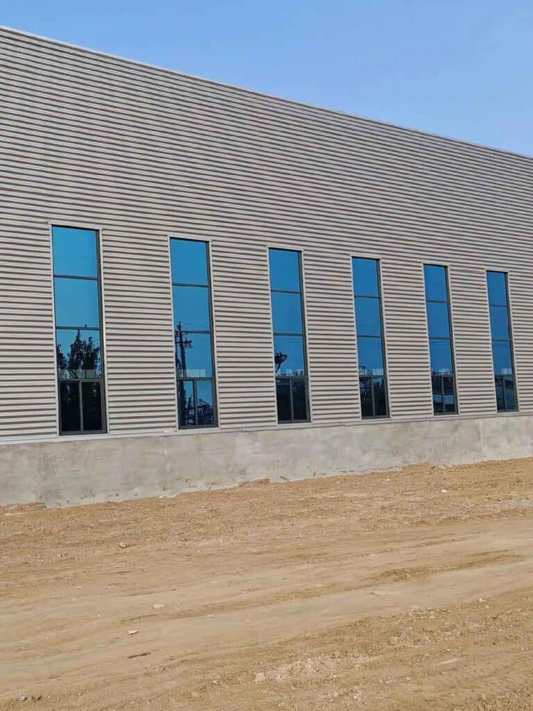 Exterior side view of a grey corrugated metal building featuring elegant blue-tinted vertical windows.