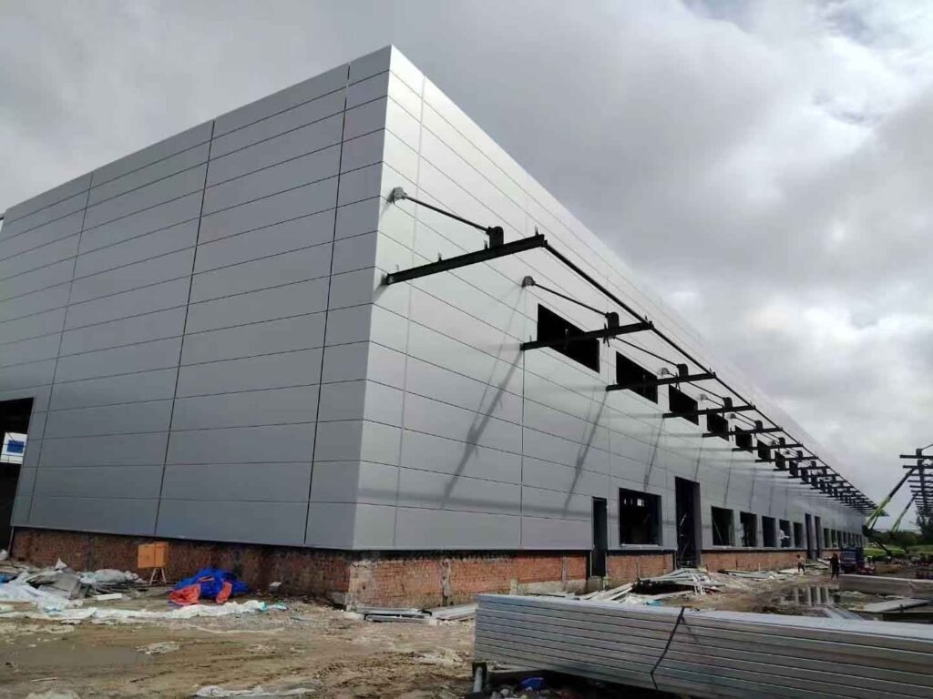 Vista panorámica del exterior de modernos almacenes industriales con enormes muros de paneles metálicos lisos grises y un esqueleto de acero continuo para marquesina.