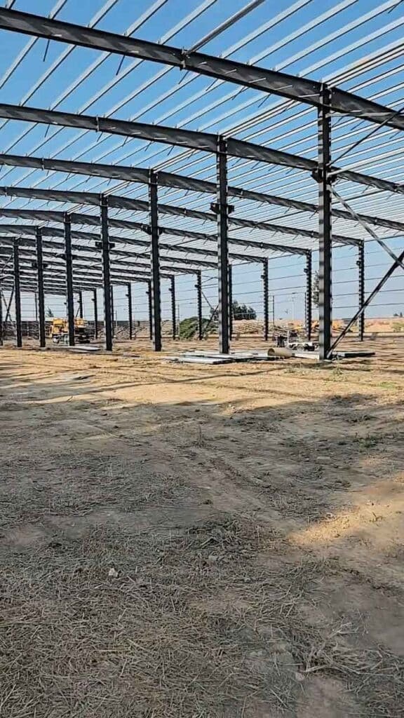 Perspectiva profunda del interior en construcción de bodegas industriales mostrando la repetición de columnas de acero sobre un vasto terreno.