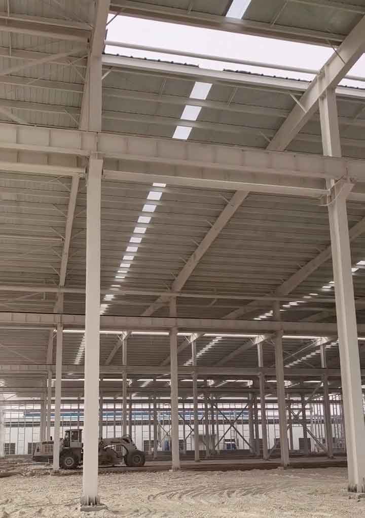 Armado de estructuras metálicas en proceso con un cargador frontal nivelando el suelo interior del galpón.