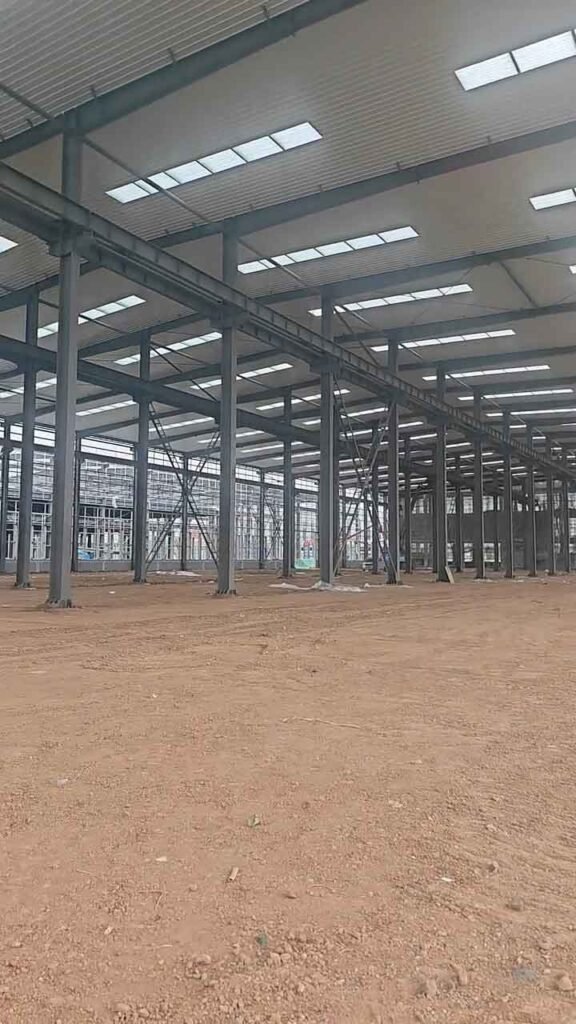 Sucesión de columnas y vigas de acero oscuro que forman el esqueleto de inmensas bodegas industriales con techo de paneles blancos y tragaluces.