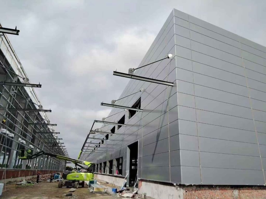 Fuerte contraste visual en la esquina de bodegas industriales prefabricadas, mostrando correas de acero expuestas junto a paneles exteriores grises lisos ya ensamblados.