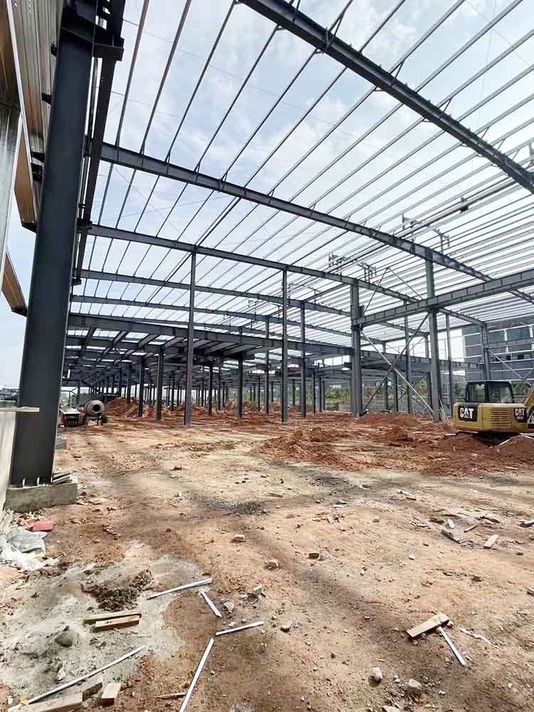 Interior construction site featuring a yellow CAT excavator preparing the ground beneath precision-engineered roof purlins provided by a top prefabricated steel building supplier.