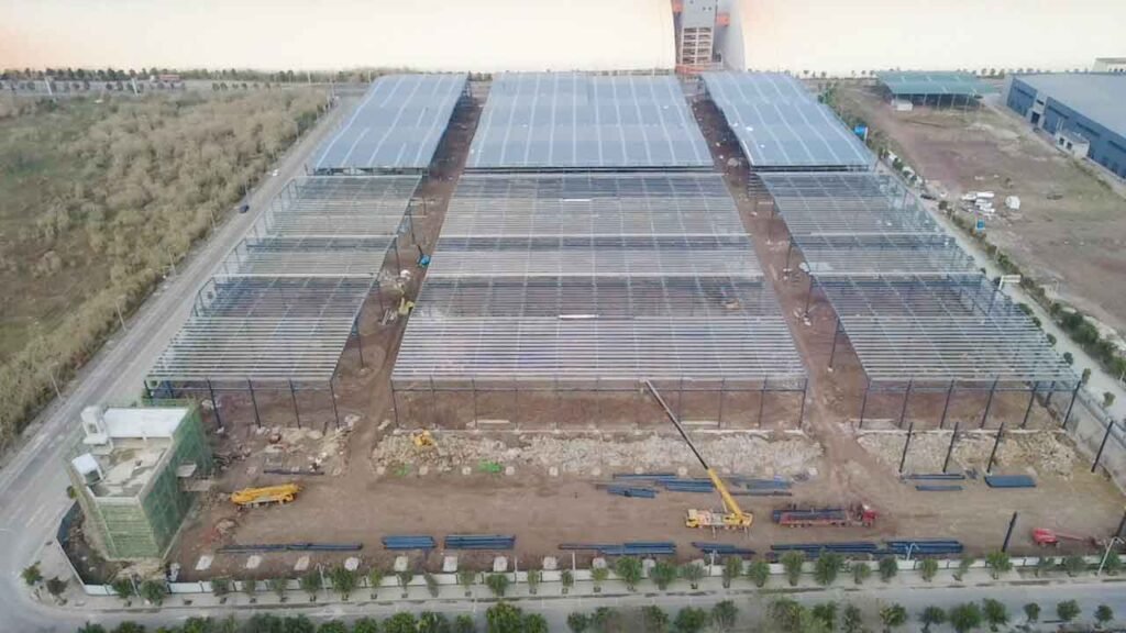 Vista frontal aérea de un complejo simétrico de ofibodegas en construcción, destacando un edificio administrativo con mallas verdes al frente.