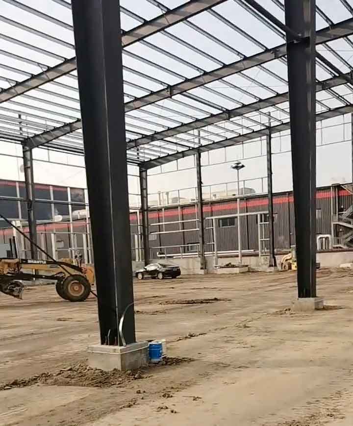 Detalle de las conexiones atornilladas en la base de grandes columnas de acero negro fijadas a pedestales de hormigón en una obra.