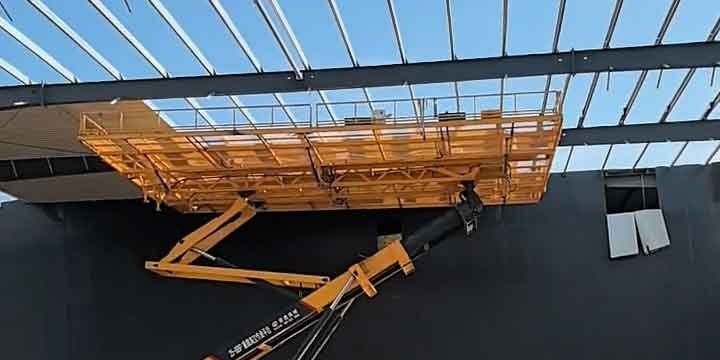 Primer plano de una amplia cesta de plataforma elevadora amarilla facilitando una construcción eficiente en la parte alta de la pared.
