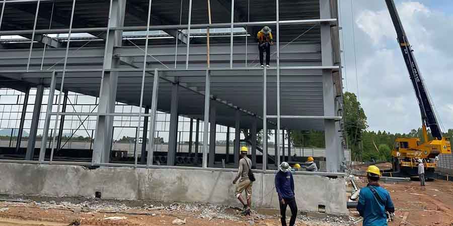 Yellow mobile crane assisting workers on the steel frame of a Metal Building, highlighting the heavy lifting required for a large metal warehouse building
