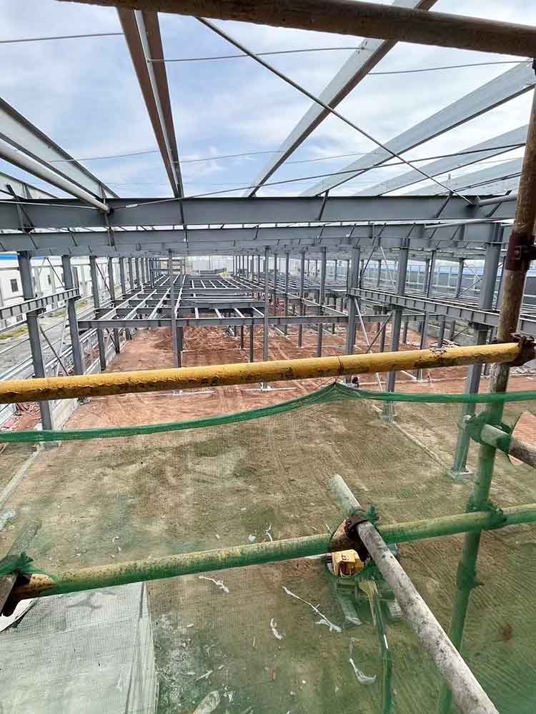 Elevated view through green safety scaffolding looking down at a densely engineered grid of structural floor joists, reflecting the high material value and steel building price Ecuador.