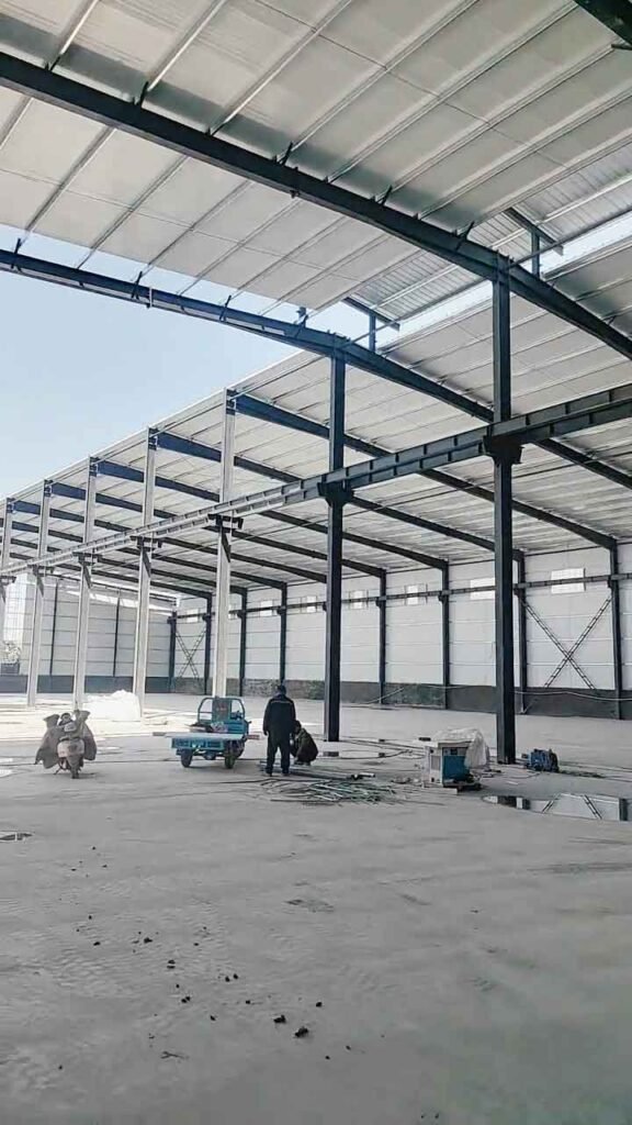 Obreros y un vehículo de carga azul trabajando en el brillante interior de un inmenso edificio de estructura de acero.