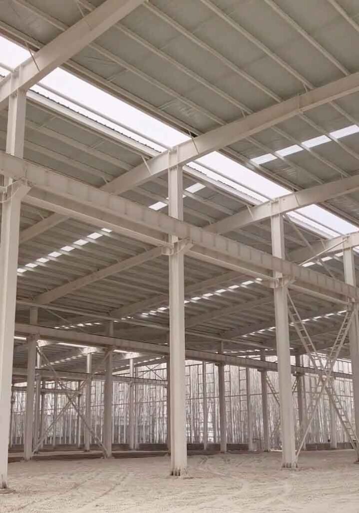 Ensamblaje de estructuras metálicas mirando hacia arriba, mostrando conexiones estructurales de vigas I y correas de techo.