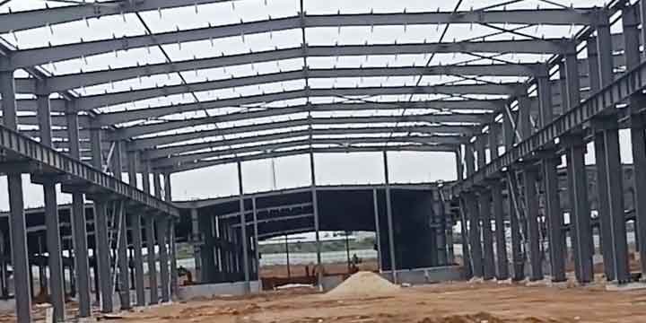 Amplia explanada interior mostrando la sucesión kilométrica de columnas y vigas de acero gris que conforman un inmenso steel structure building en etapa de montaje.