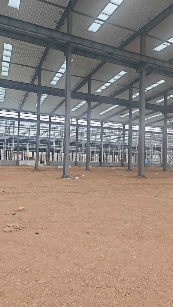 Amplia estructura metálica de color gris oscuro ensamblada sobre un terreno arcilloso, mostrando el cerramiento superior con iluminación natural y vanos laterales.