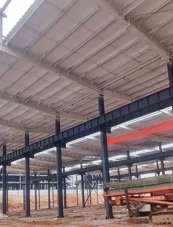 Plataforma de tijera color naranja trabajando en las estructuras metálicas del techo de una gran nave con piso de tierra y zócalos perimetrales.