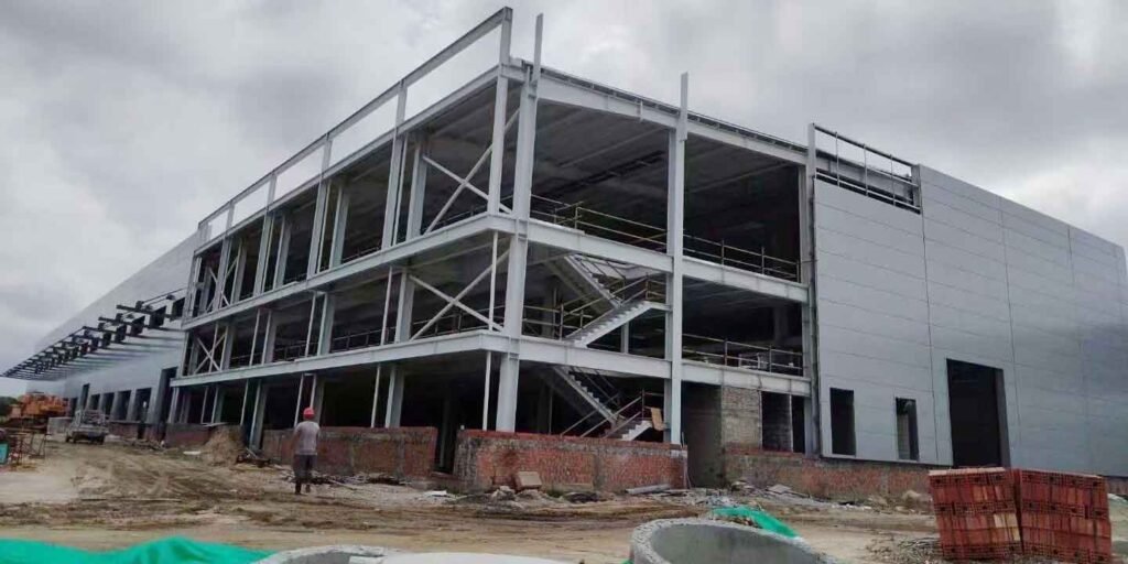 Sitio de construcción de nave industrial de estructuras metálicas de múltiples niveles con escaleras prefabricadas de acero integradas y muro base antivuelco de ladrillo rojo.