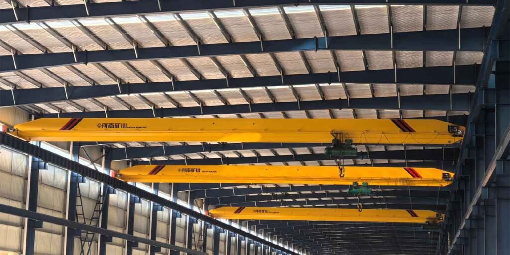 Múltiples puentes grúa alineados bajo el techo de una nave industrial construida por un fabricante de estructuras metálicas integrales.