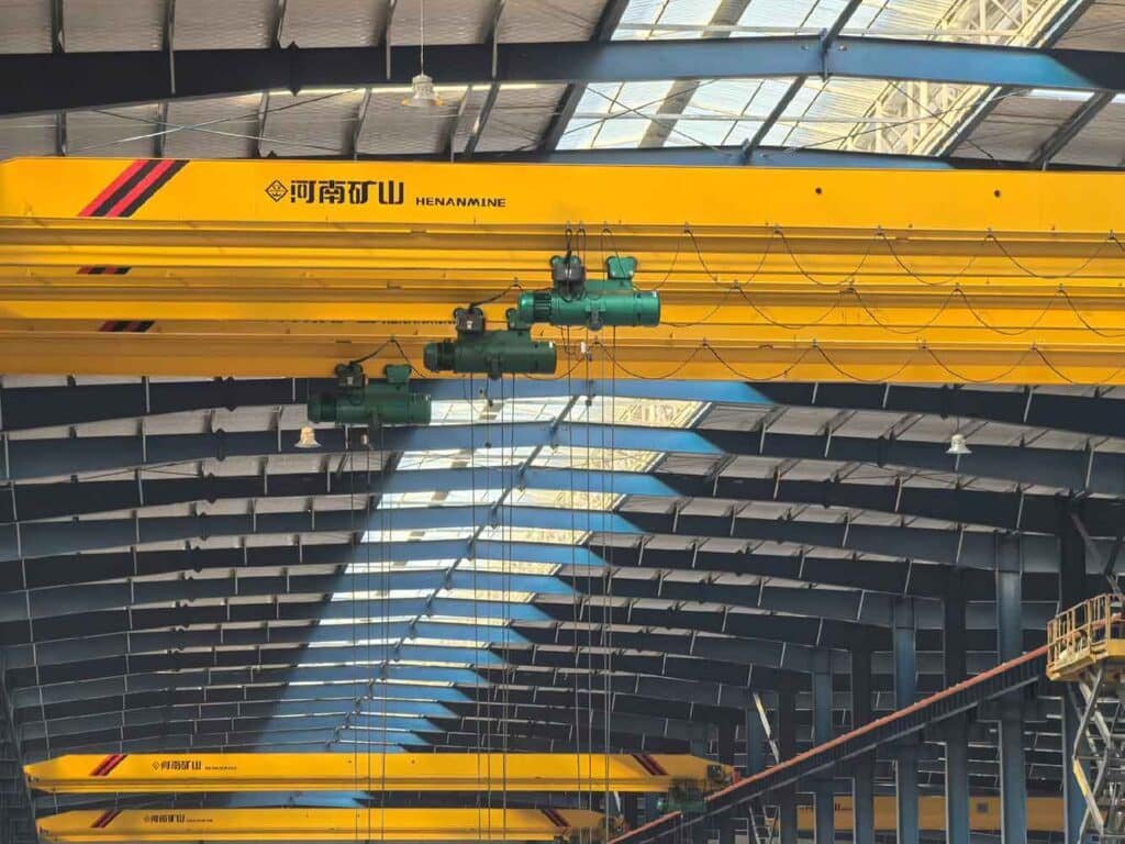 Detalle de puentes grúa amarillos y polipastos soportados por vigas carrileras de un fabricante de estructuras metálicas pesadas.