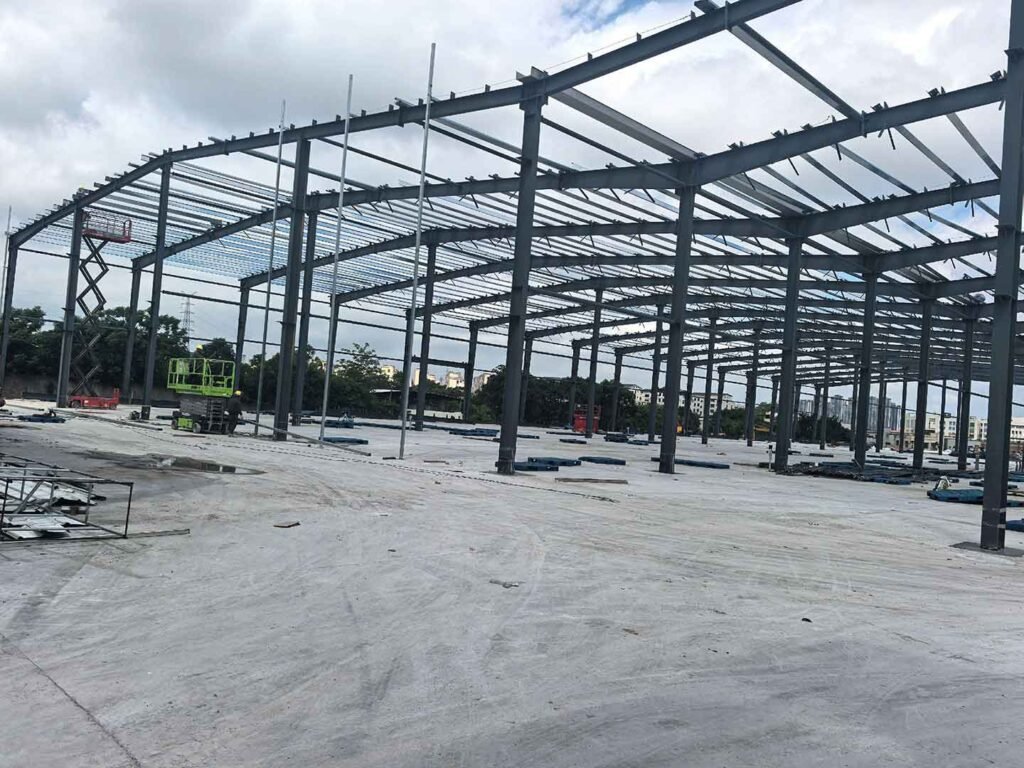 Vista panorámica de un galpón metálico en construcción sobre losa de concreto, destacando plataformas elevadoras tijera roja y verde para montaje en altura