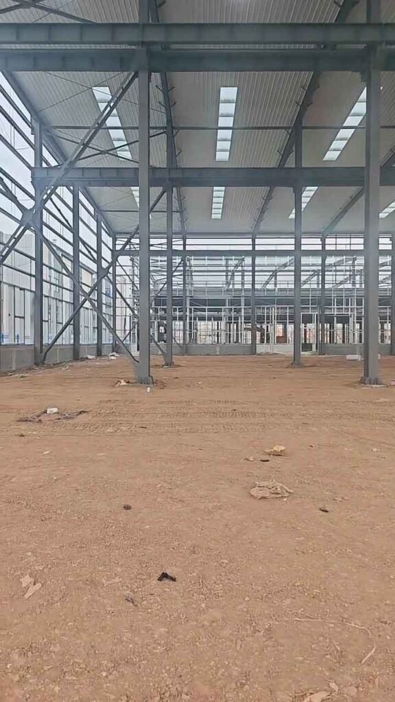 Detalle de los arriostramientos cruzados en las paredes laterales de galpones metálicos en fase de obra, sostenidos por gruesas columnas grises.