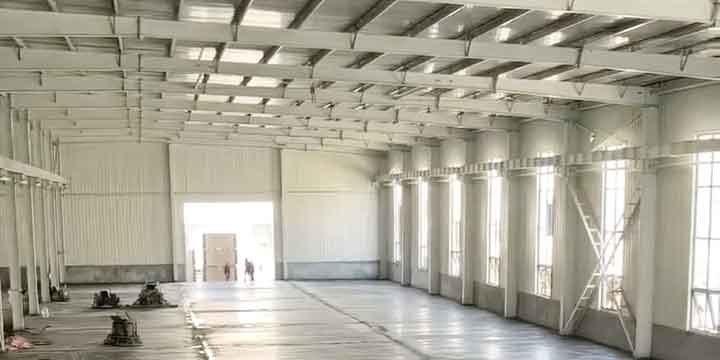 Amplio espacio interior con vigas de techo y columnas blancas apuntando hacia una gran puerta iluminada al fondo en bodegas de almacenamiento.