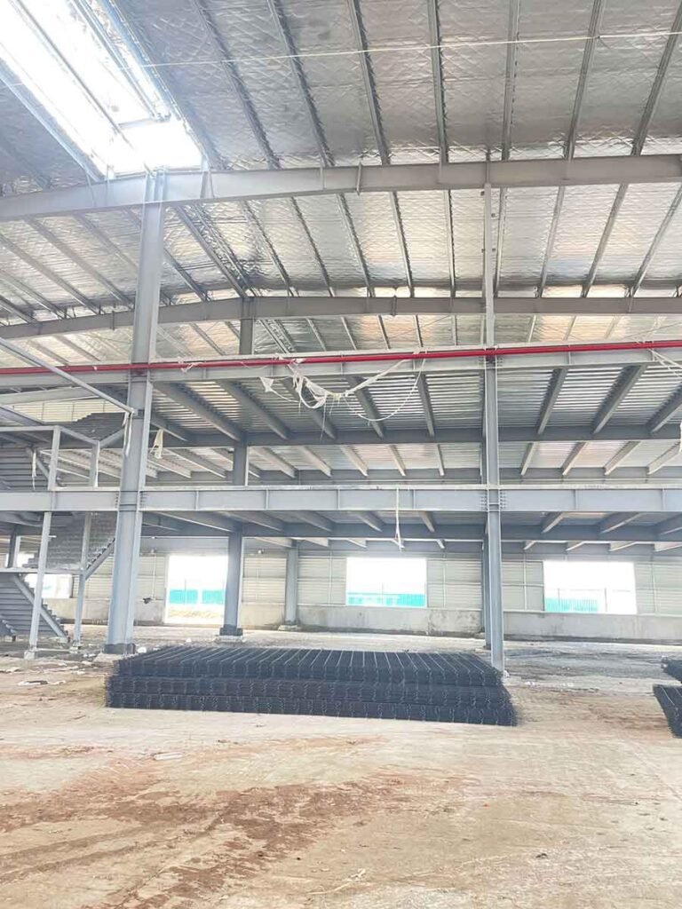 Interior view of a Metal Building featuring a constructed mezzanine level, roof insulation, and red fire safety pipes, typical of a modern steel structure warehouse.