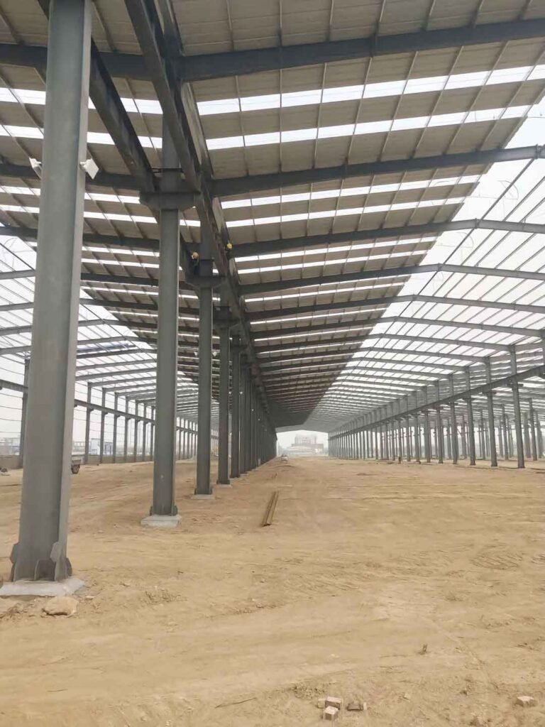 Grúa industrial elevando paneles sándwich azules hacia el techo durante la construcción de un depósito logístico aduanero