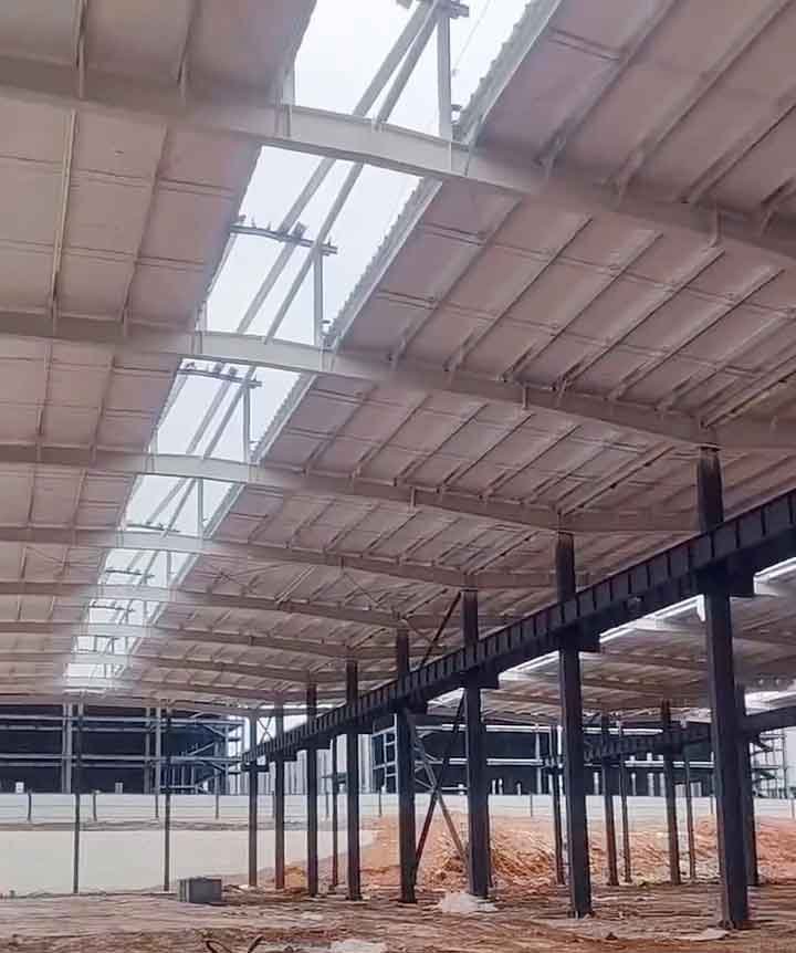 Perspectiva interior de una maestranza metalmecánica en construcción con gruesas columnas negras y entramado de techo blanco sobre suelo de tierra arcillosa.