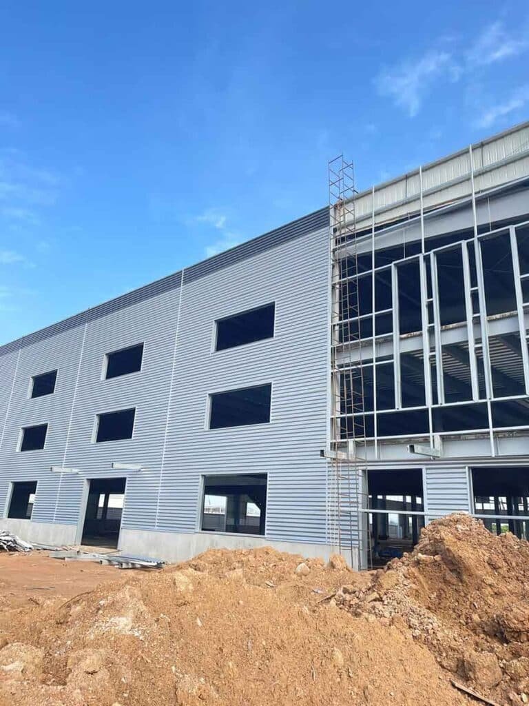Half-clad exterior facade of a Metal Building showing grey corrugated panels and exposed steel framing, highlighting the precision materials provided by a steel building supplier.