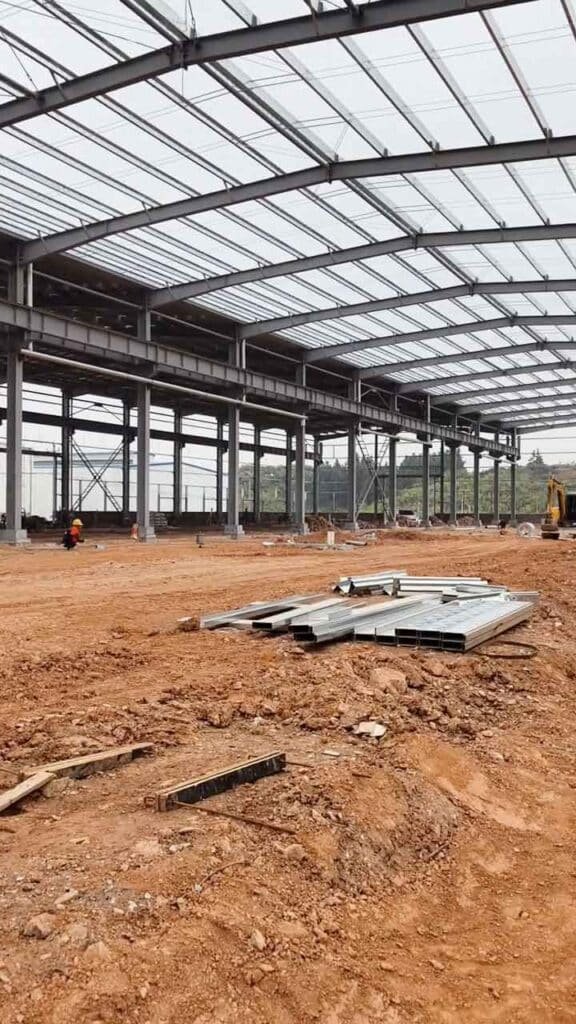 Interior de nave demostrando una construcción eficiente con muros de ladrillo rojo, ventanas superiores y tensores de acero en cruz en la estructura de soporte.