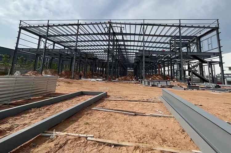 Wide exterior view of a multi-bay skeletal frame with a mezzanine level and scattered foreground steel beams, typical of a high-capacity steel structure warehouse Ecuador.